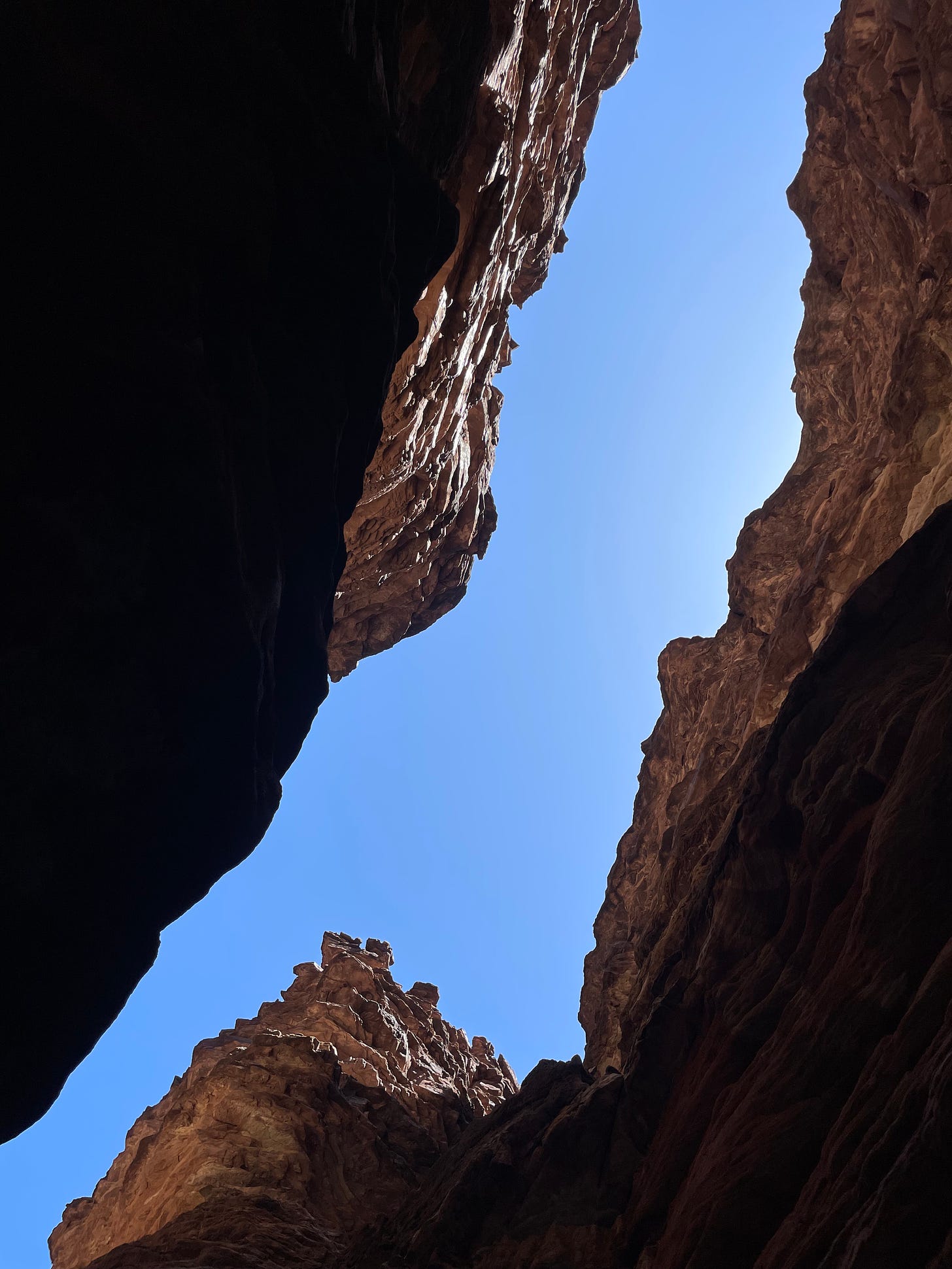 A view looking up through a narrow slot canyon, with a slit of blue sky visible between two wedges of tall, pink rock