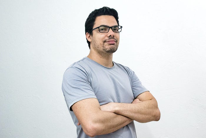 a confident young man wearing glasses and crossing hands with a gray casual t-shirt