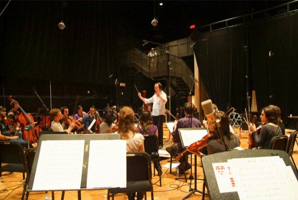 A picture of the author standing in front of a small orchestra, arms raised in conducting position, about to bring the musicians in for a pass at recording one of his cues.