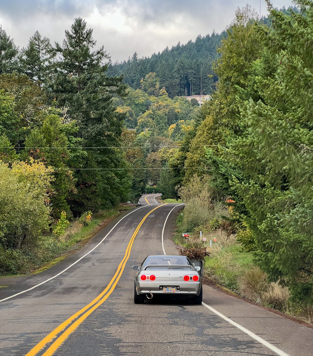 Rear view of a grey Nissan R32 Skyline GT-R driving backroads through rural Oregon. Photo by Ryan ZumMallen, author of 'Cult of GT-R.'