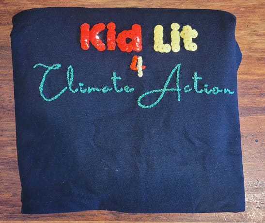 folded black tshirt with sequined and embroidered words Kid Lit 4 Climate Action