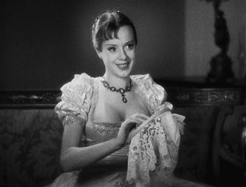 Animated gif. Elsa Lanchester as Mary Shelley. She’s on a fancy sofa embroidering