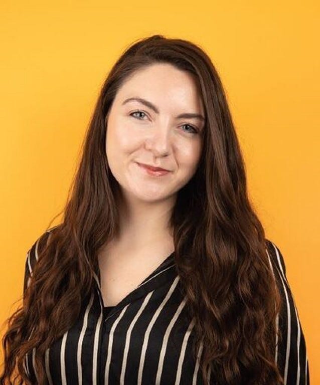 Headshot of a white-skinned woman with dark brown hair wearing a black and white striped shirt, posing against an orange background