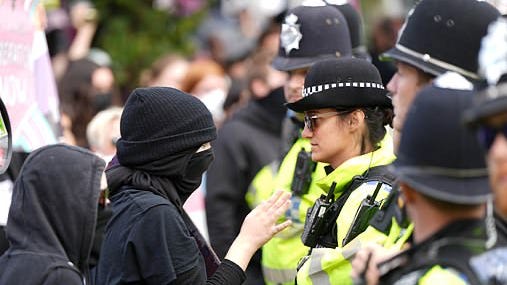 A person wearing a black mask and a black hat with a police officer

Description automatically generated