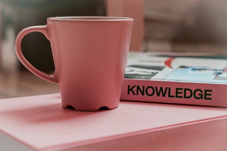 A pink cup in front of a book spine titled knowledge.