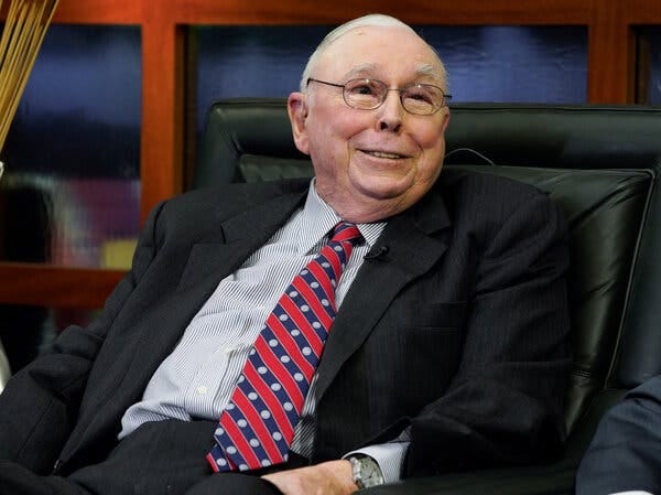 Mr. Munger was photographed smiling as he sat in a black leather office chair. He wore a charcoal-gray suit and a red patterned necktie. 