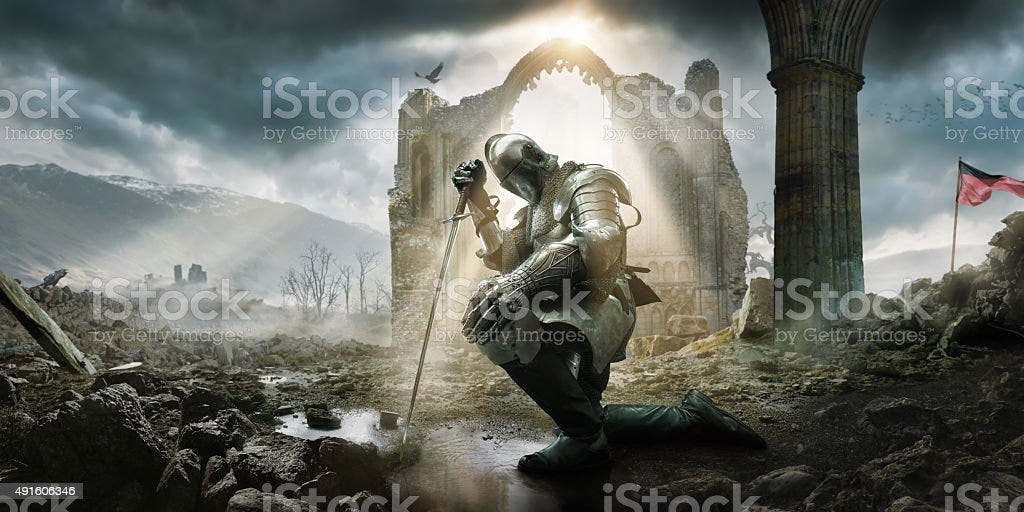 Medieval Knight Kneeling With Sword In Front of Building Ruin A Medieval knight wearing full suit of armour, boots and chainmail, kneeling as if in defeat or contemplation in preparation for battle. He rests on his sword in a puddle amongst rocks and rubble in front of a building ruin under a dramatic stormy evening sky with rays of sunlight. Knight - Person Stock Photo