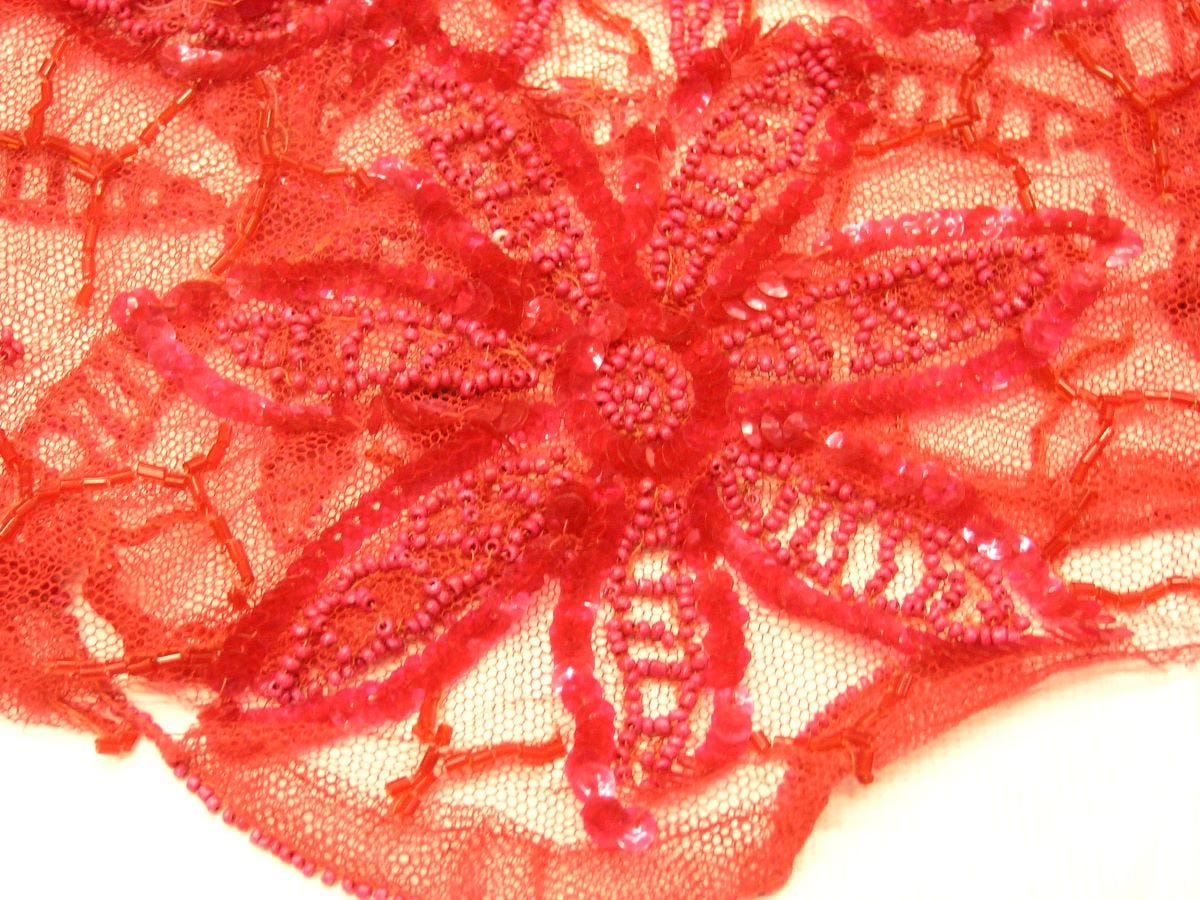 Detail of a red lace, bead and sequin flower from a dres