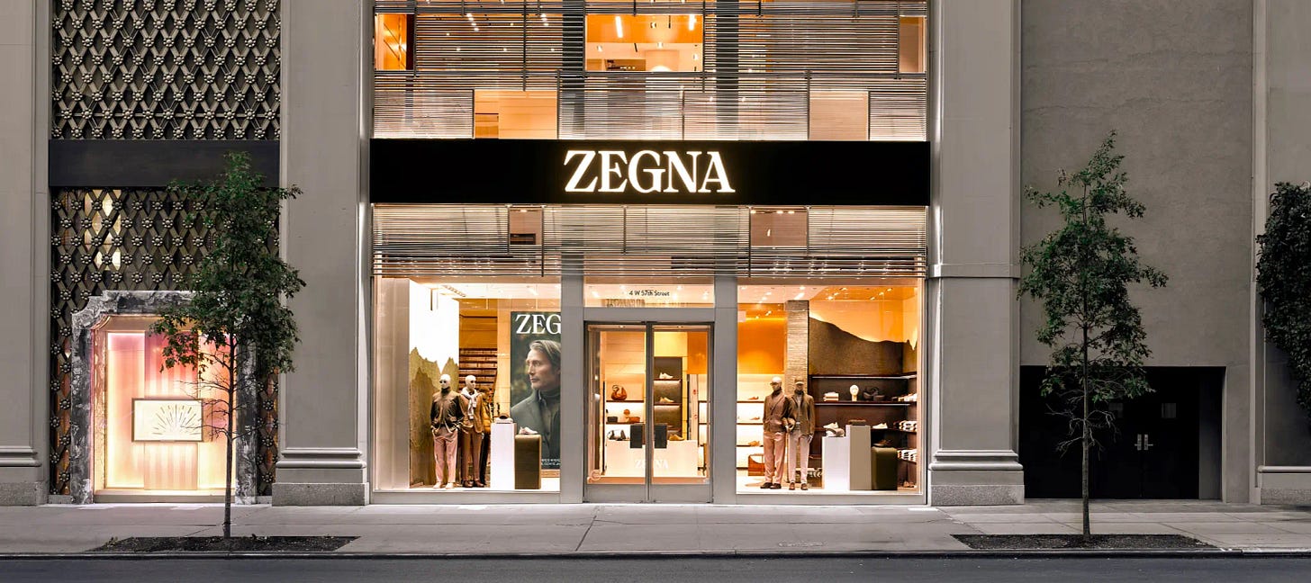 Exterior of ZEGNA luxury boutique with illuminated sign and window display featuring the new collection.