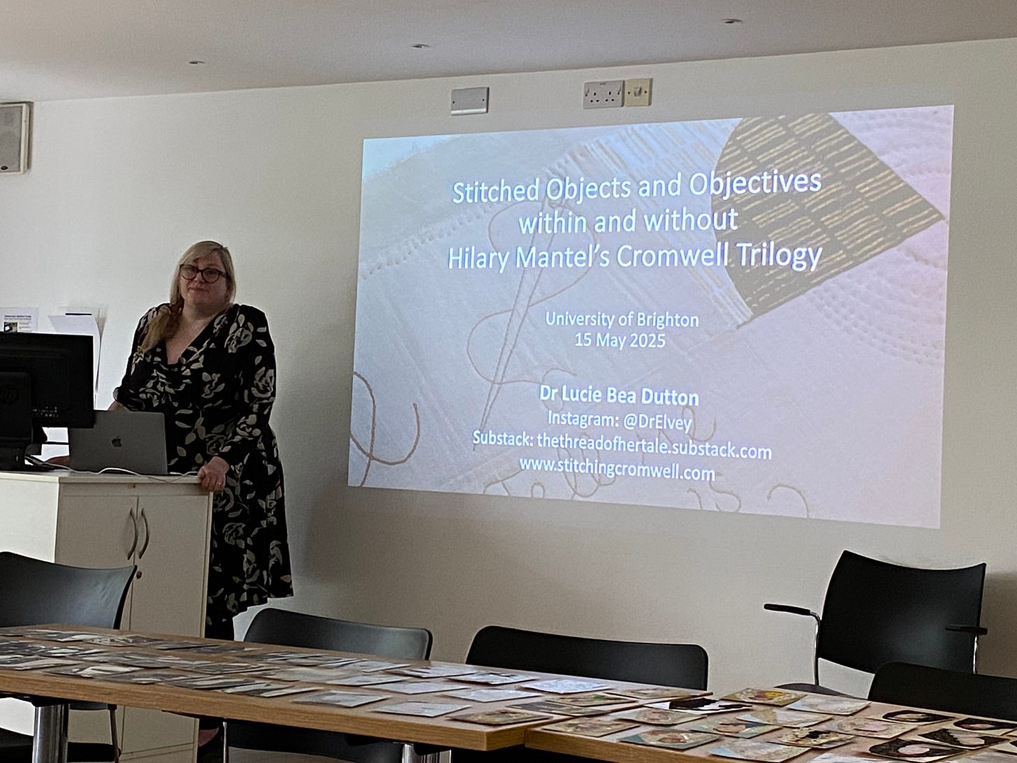 A white woman standing in front of a screen that reads “Stitched Objects and Objectives within and without Hilary Mantel’s Cromwell Trilogy”