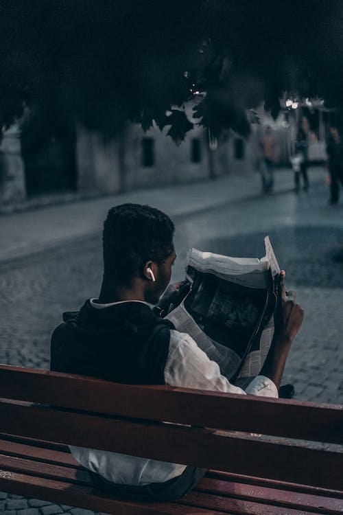Free Man Reading a Newspaper Sitting on Wooden Bench Stock Photo