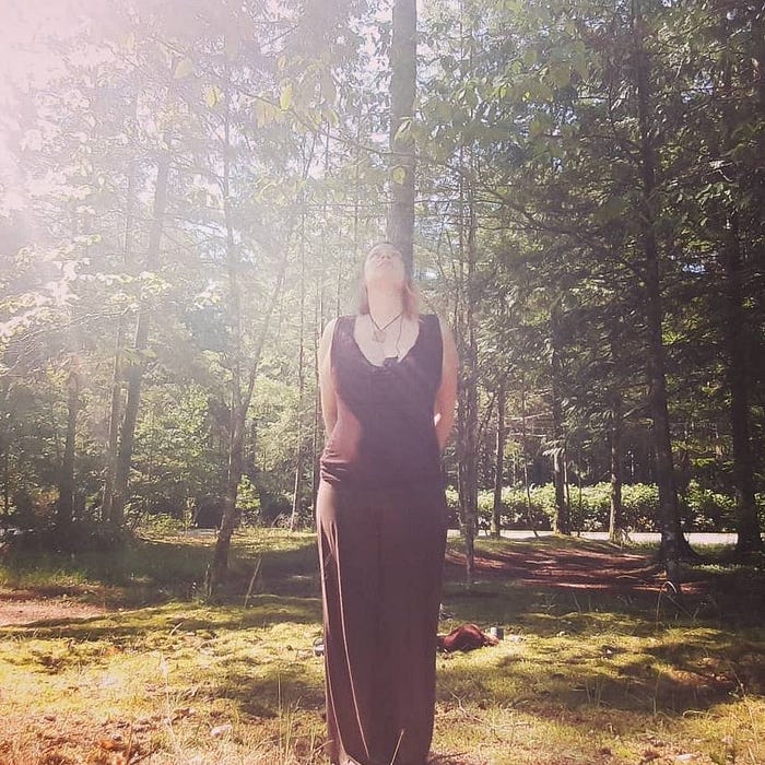 Juliette Jarvis, the author, standing straight in a forested setting and looking up to the sky