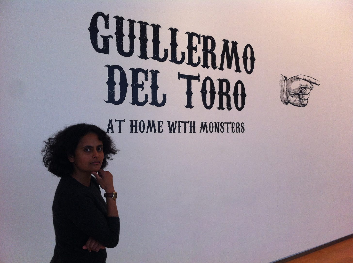 Me standing in front of a wall-sign: “Guillermo del Toro: At Home with Monsters.”