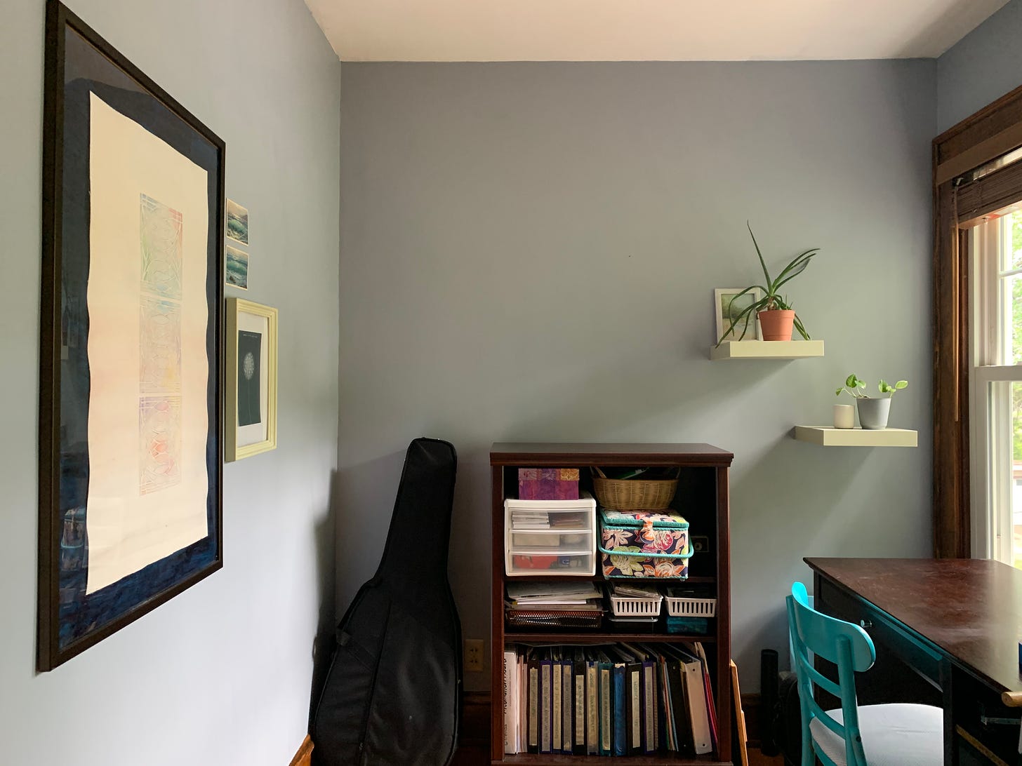 A small room with art on the wall plus a book case and desk.