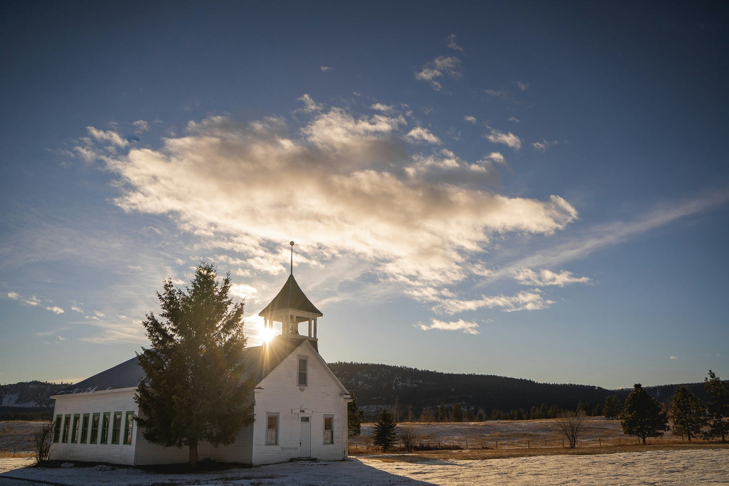 Image of rural church with sun shining from behind through steeple.