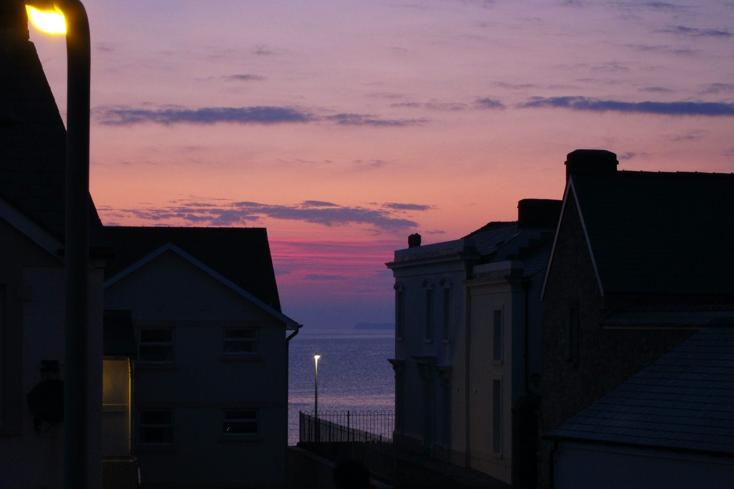 Sea view between buildings as darkness sets in. The sky has shades of pink and lavender
