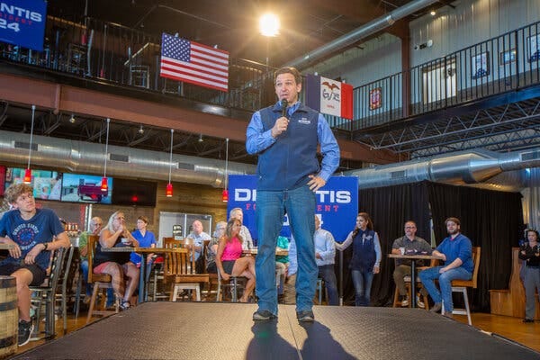 Gov. Ron DeSantis speaking onstage at a brewery in Iowa. People in the background are listening.