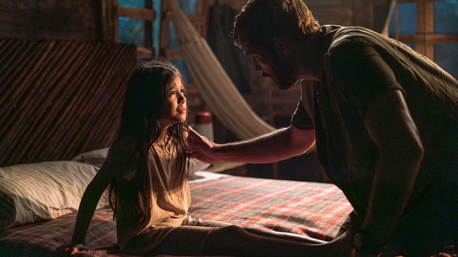 This is a screenshot of the movie "Sound of Freedom." In the darkened screencap, Jim Caviezel (portraying Tim Ballard) is seen touching the shoulder of a young girl sitting on the bed look up at him.