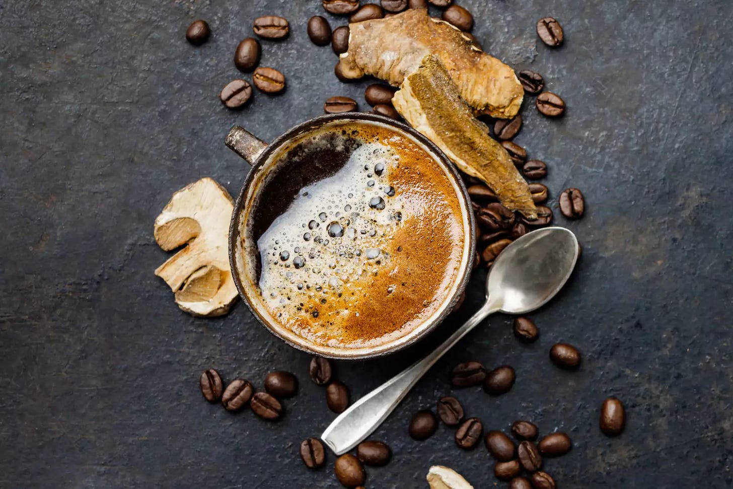 a photo of a cup of coffee with mushrooms and coffee beans surrounding it