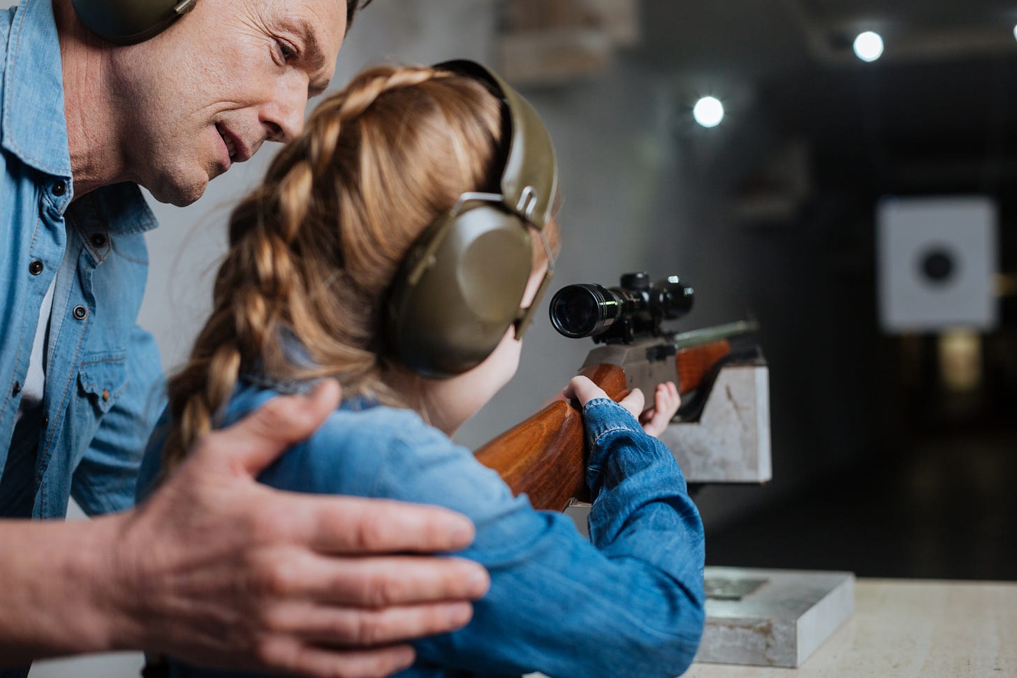 Color photo of man teaching young girl to shoot rifle