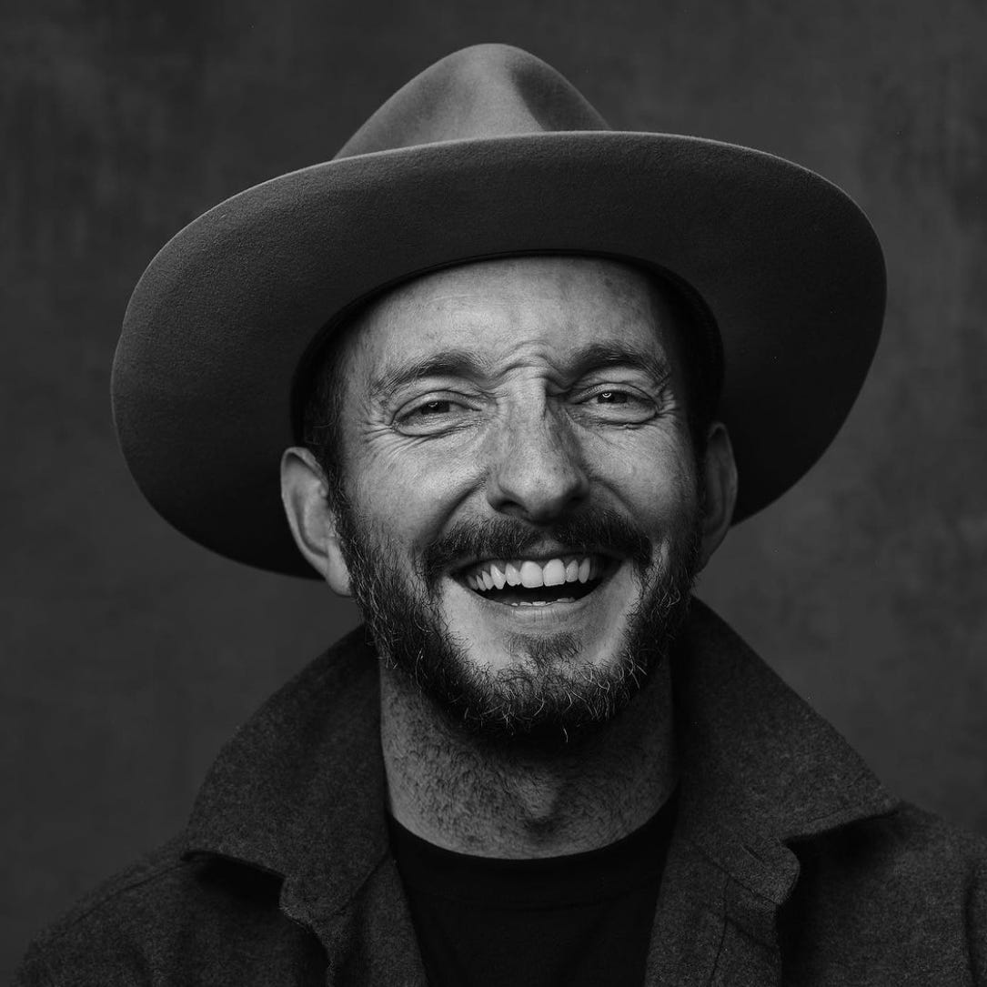 A greyscale photograph of Jedidiah Jenkins in a wide brimmed hat, his face crinkled in laughter