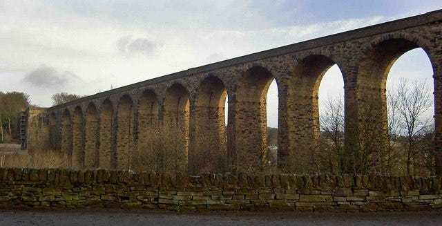 a stone viaduct across a valley with a wall in front of it
