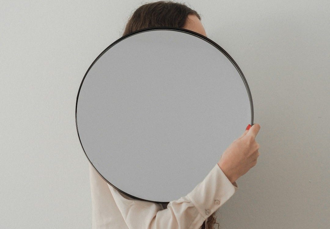 person holding round mirror with white frame