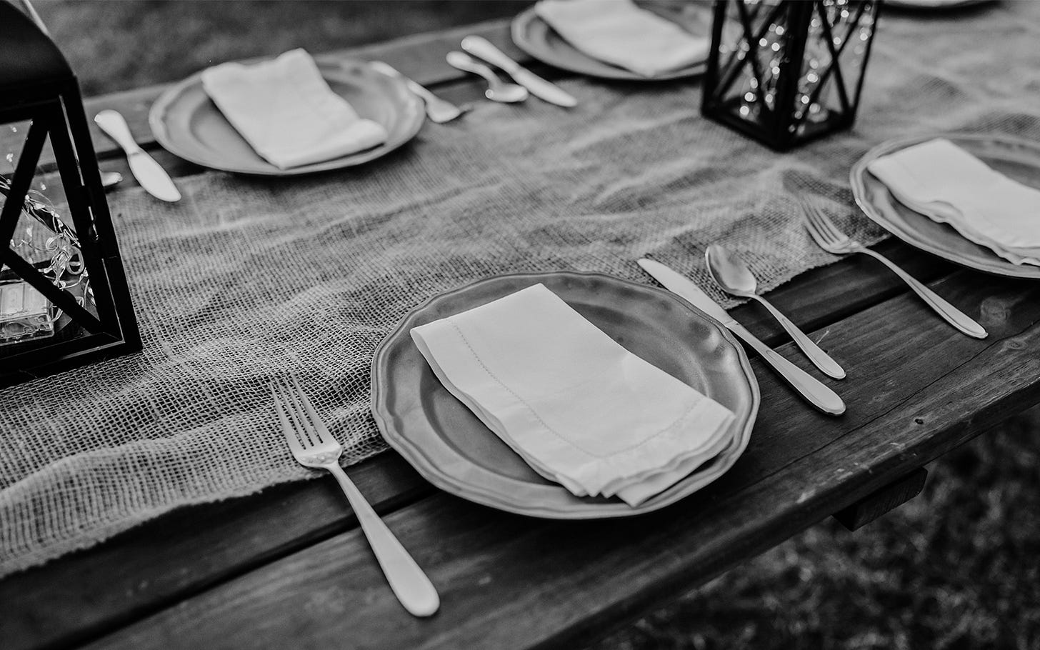 Wood table set with plates, silverware and napkins. A corse fabric runs down the middle of the table.