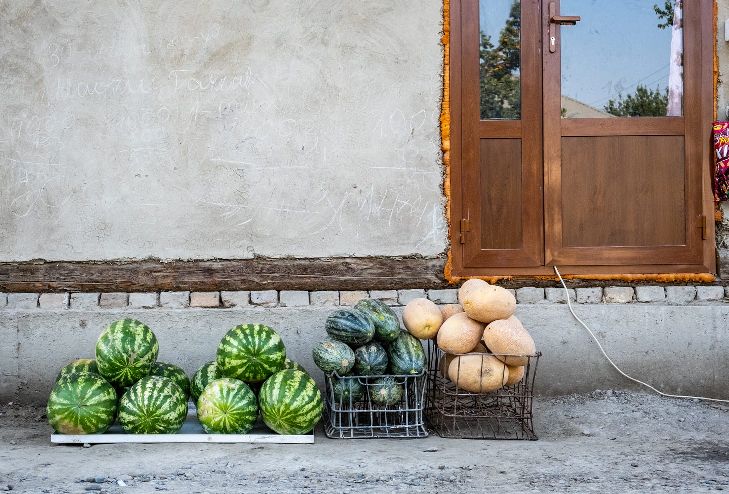 A display of watermelon sits next to two other types of melons in wire crates.