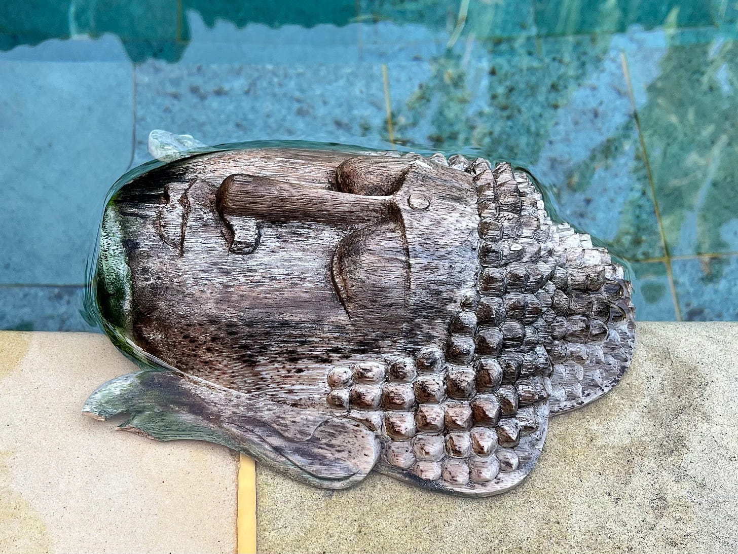 A wooden mask on a pool rim