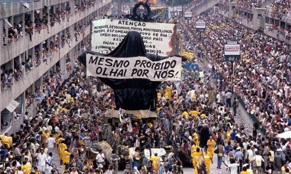 imagem colorida de um destile da Beija-flor em que uma est[atua de Cristo Redentor foi censurada e acabou entranco coberta por uma imenso saco preto com os dizeres: mesmo proibido olhai por nós