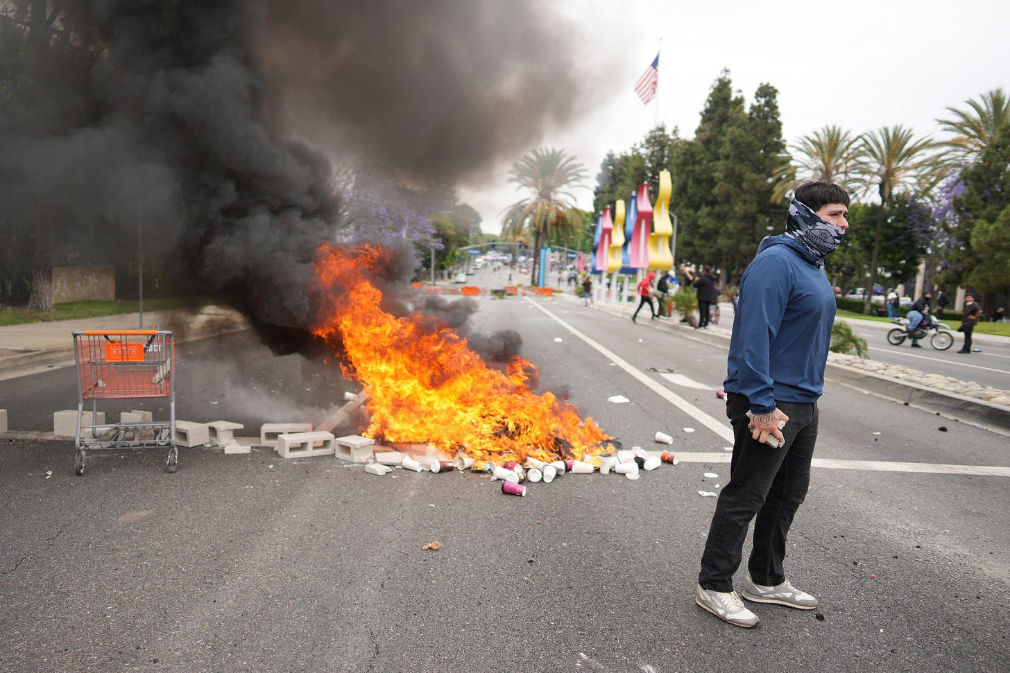 A fire burns as a protester confronts law enforcement personnel in riot gear and gas masks during a demonstration over dozens of people detained in an operation by ICE agents a day earlier in the Paramount area of Los Angeles A fire burns as a protester confronts law enforcement personnel in riot gear and gas masks during a demonstration over dozens of people detained in an operation by ICE agents a day earlier in the Paramount area of Los Angeles