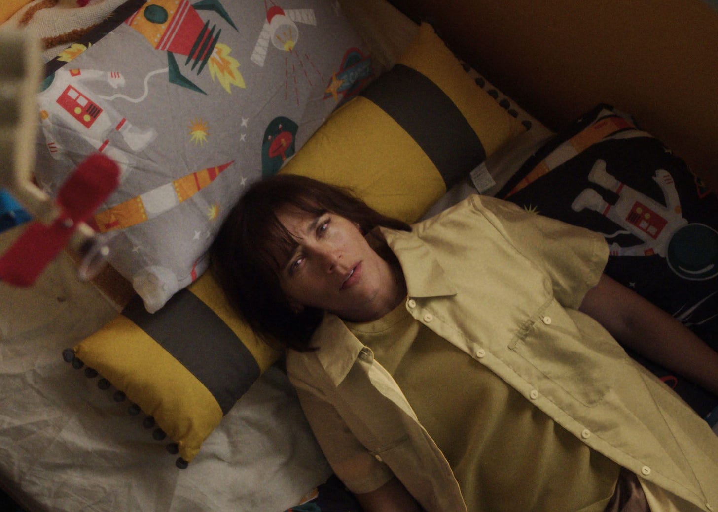 Rashida Jones as Suzie in "Sunny" lying in bed wearing a yellow shirt over a t-shirt