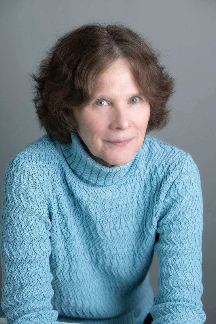 A photo of a woman with reddish brown hair in a light blue sweater, leaning slightly toward the camera