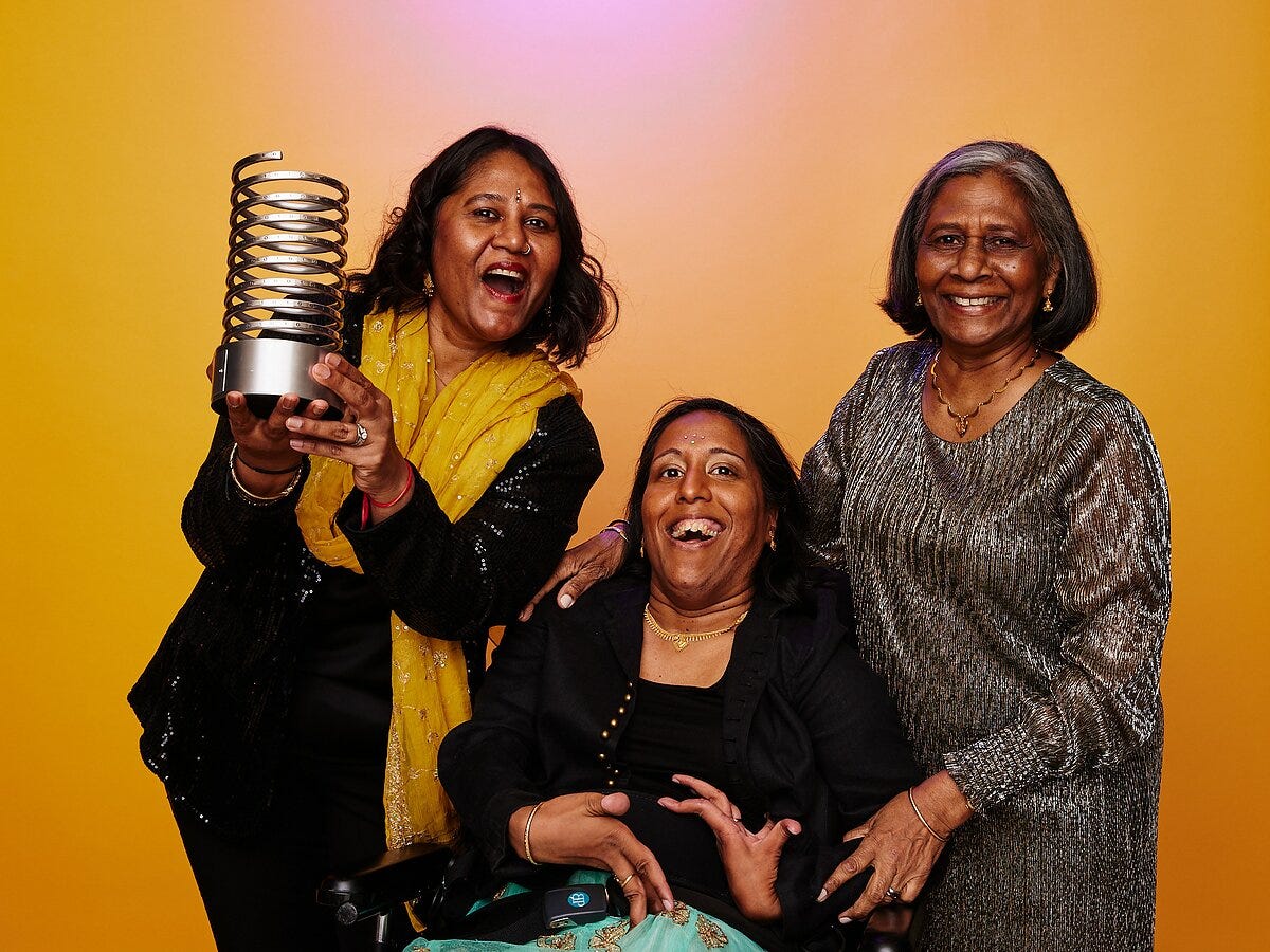 Lakshmee Lachhman-Persad (left) holding a Webby Award, accompanied by her sister (center) and mother (right).