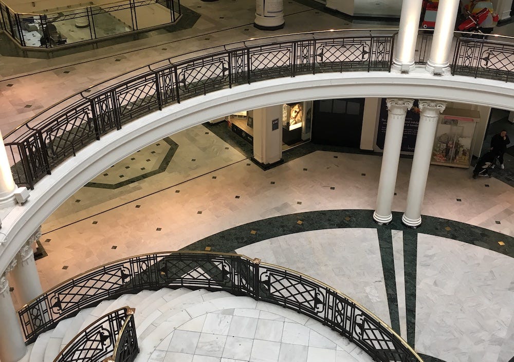 A photograph I took in March 2017, of the Whiteleys shopping centre in Bayswater. You can see the atrium, and a spiral staircase, object in beautiful black and white tiling, with brass railings.