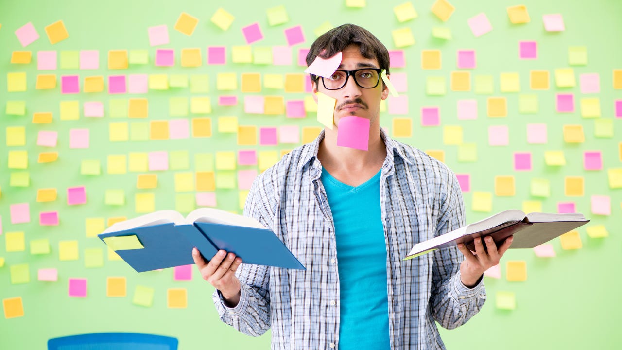 A man holding to books while covered in sticky notes.