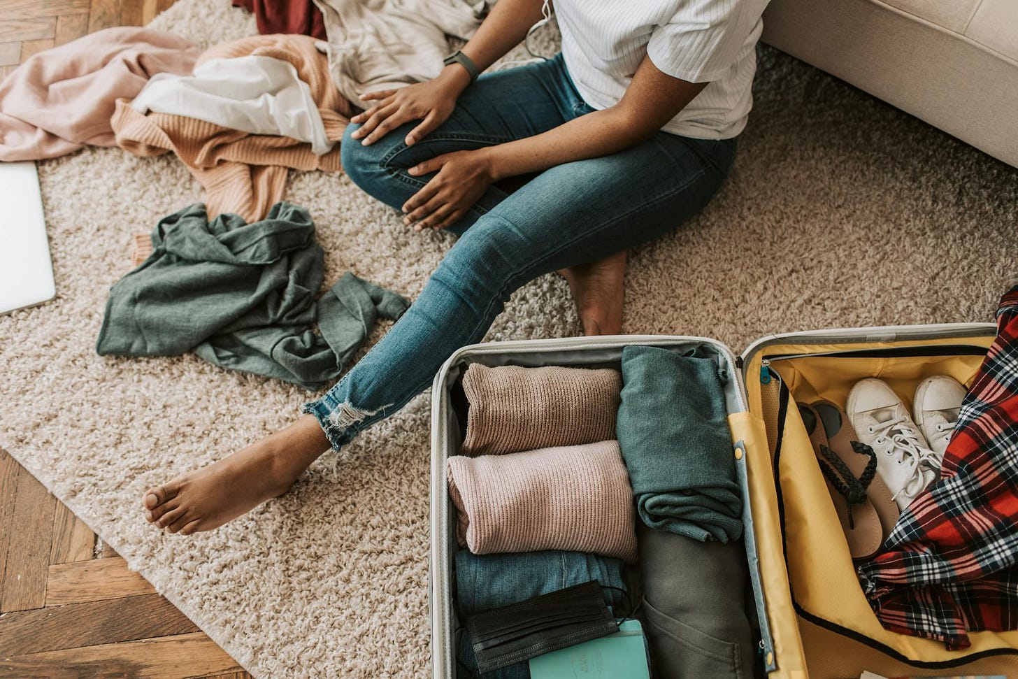 Woman packing a suitcase with clothes sprawled out on the floor around her