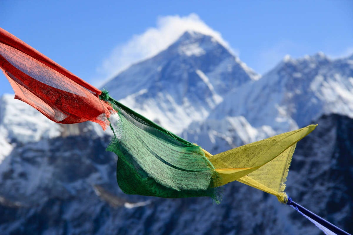 tres banderas roja, verde y amarilla sobre un fondo en el que se ve la cordillera del Himalaya nevada
