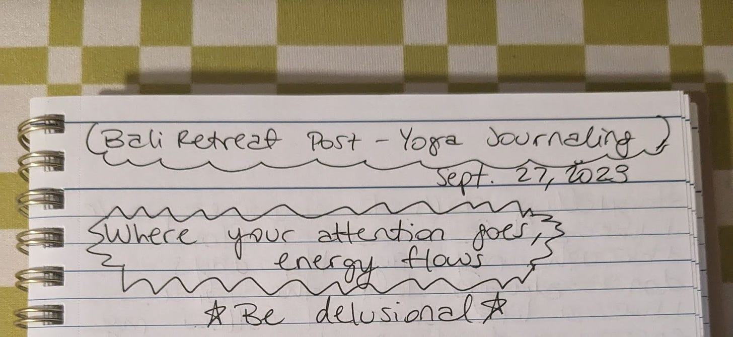 A notebook with text that reads, "Bali Retreat Post-Yoga Journaling. Sept. 27, 2023. Where your attention goes, energy flows. Be delusional"