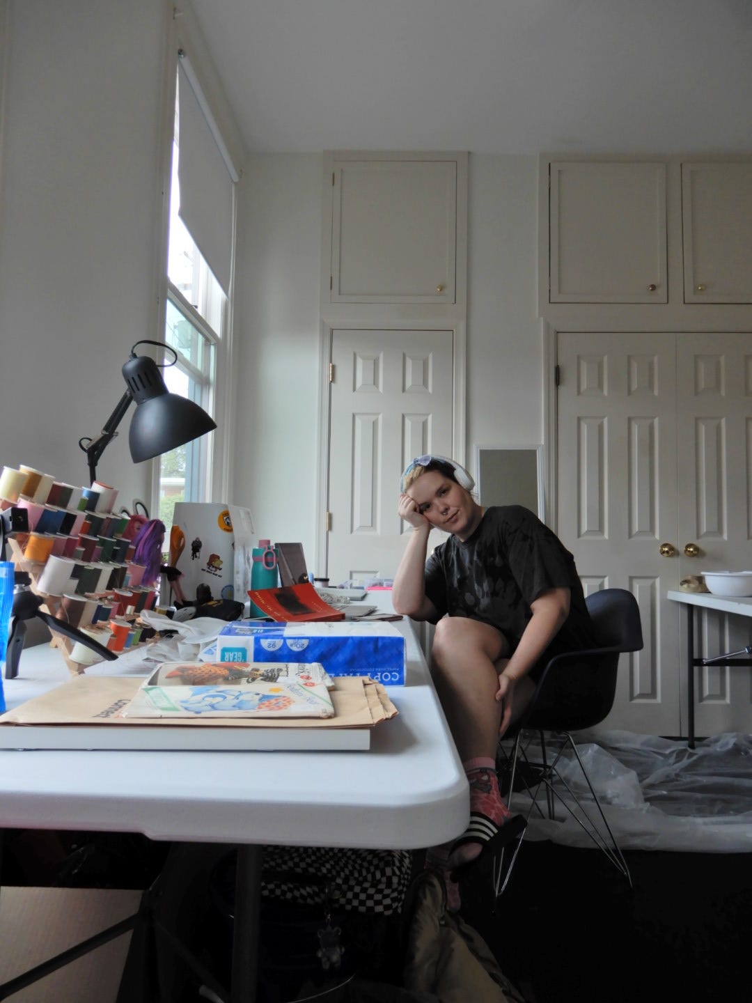 shelby sits at a cluttered desk in front of a white wall of doors