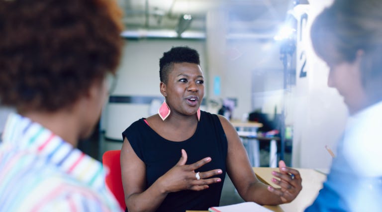 A woman facing two people talking them with her hands