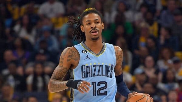 Ja Morant, his hair pulled back in a ponytail and wearing a blue Memphis Grizzlies jersey, dribbles the basketball with his left hand during a game.