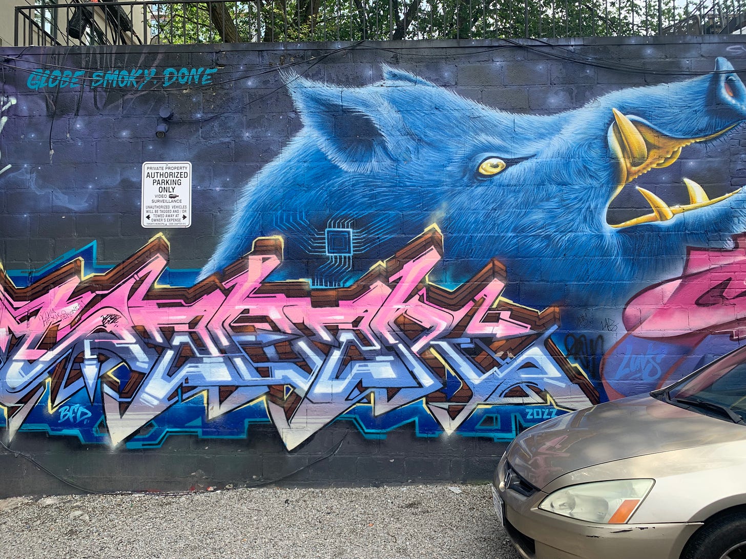 A mural with a blue and pink metallic-looking tag reminiscent of 80s/90s video game art with the head of a blue pig with gold teeth in the background, floating in space.