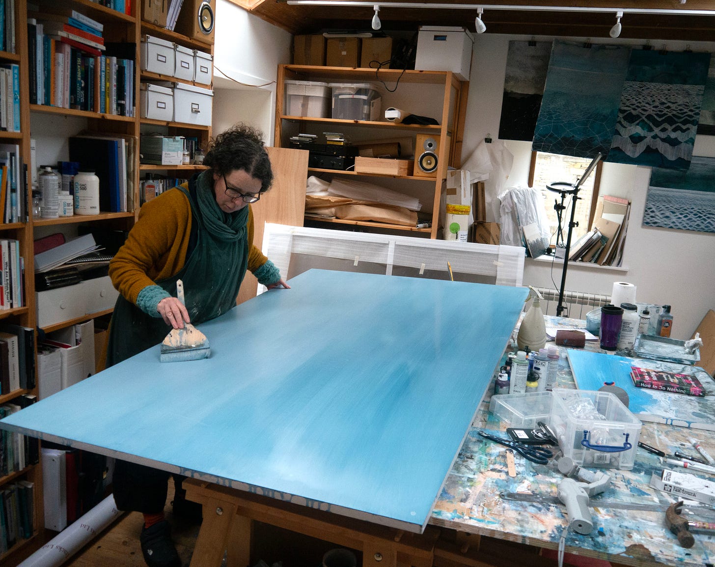 The artis painting a layer of blue onto a large panel laid over a workbench