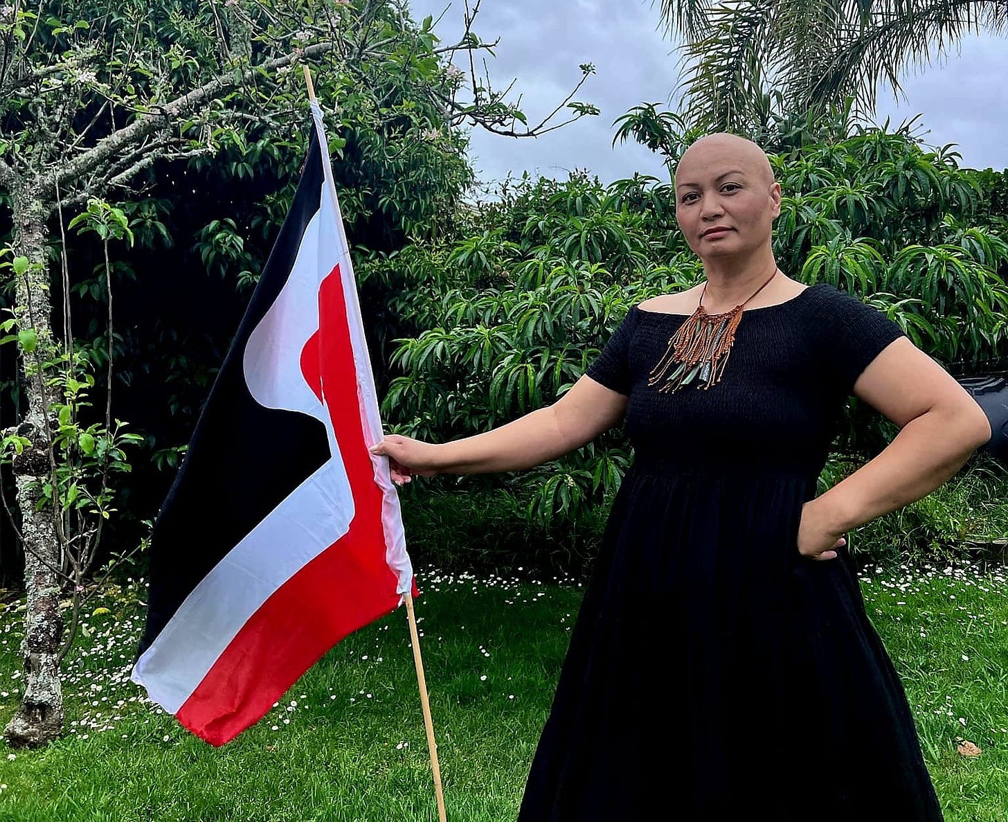 Marama Davidson holds a Māori flag in a garden.