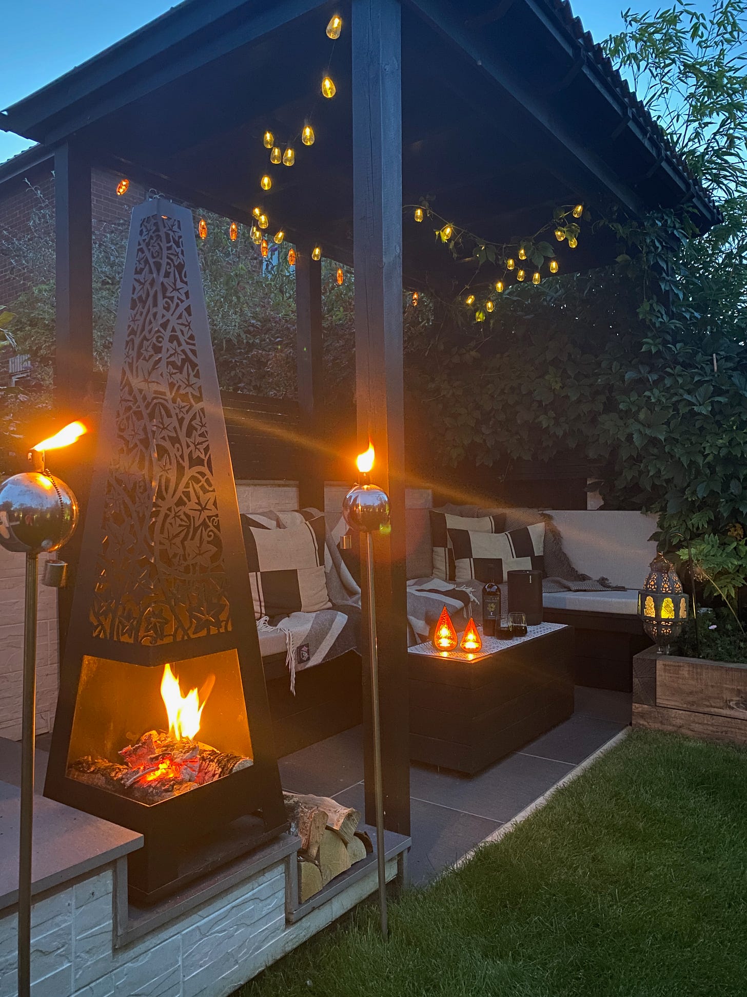 pergola area at dusk lit up with festoon lights and the chiminea lit