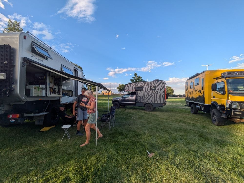 three uniquely styled camper rigs with people milling about on the green grass