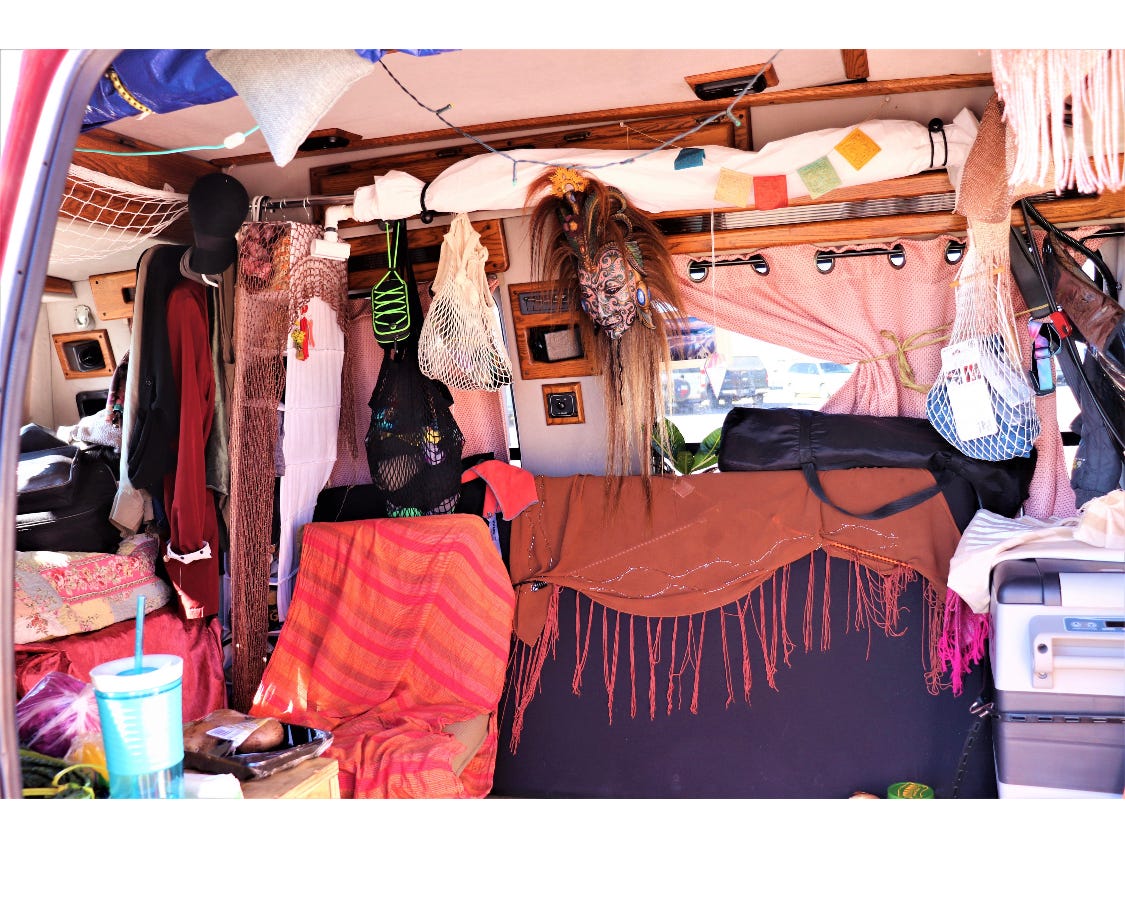 The inside of a DIY van with brightly colored throws, a mask from Indonesia, prayer flags, and hanging netted bags.