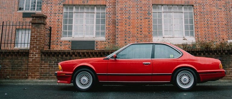 red coupe parked beside brown building